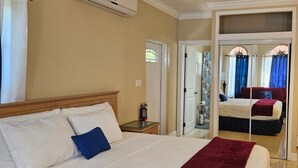 A hotel room with a bed, bedside table, and an air conditioning unit. - Casa de Bells 2 - Studio apartment with pool, gazebo, private entrance & parking (George Town)