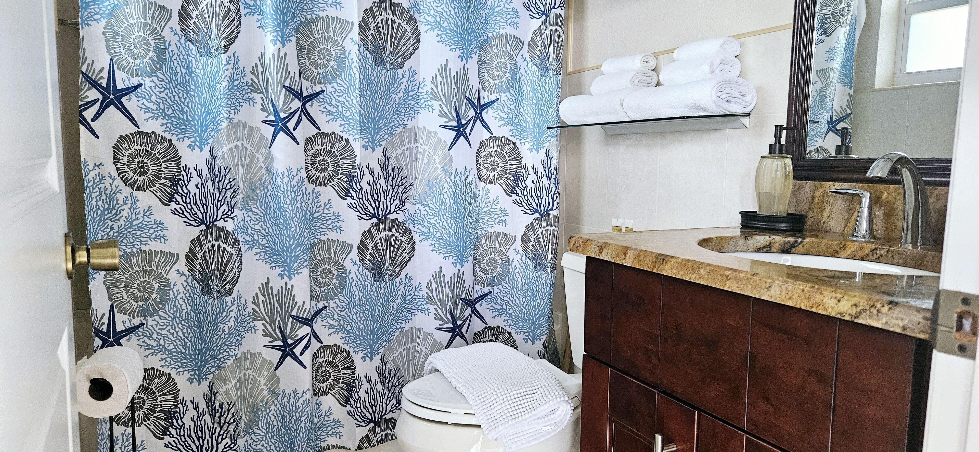 A bathroom with a shower curtain featuring a sea life pattern, a sink with a mirror, and a towel rack above the sink.