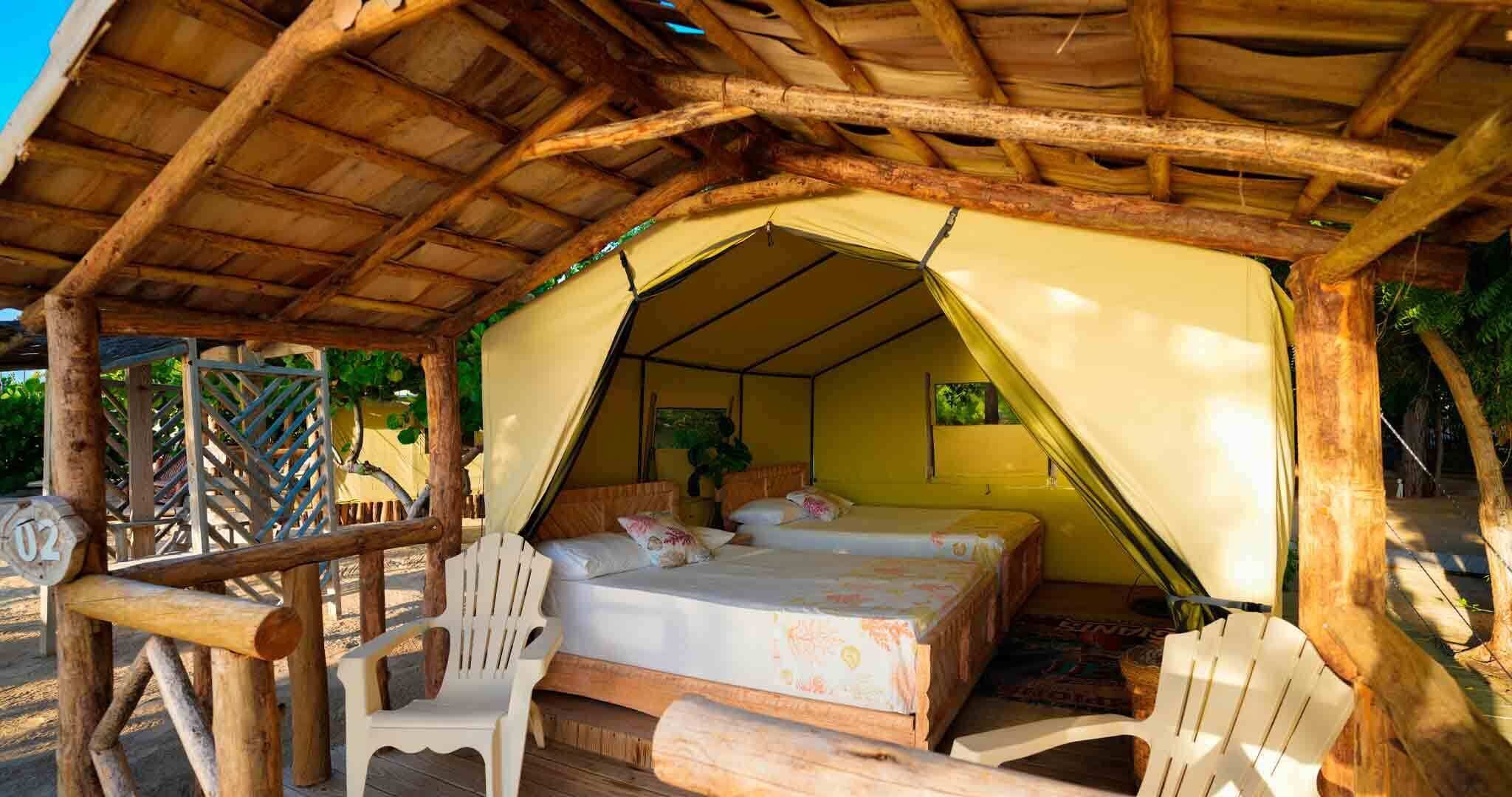A tented accommodation with a bed, two chairs, and a wooden deck.