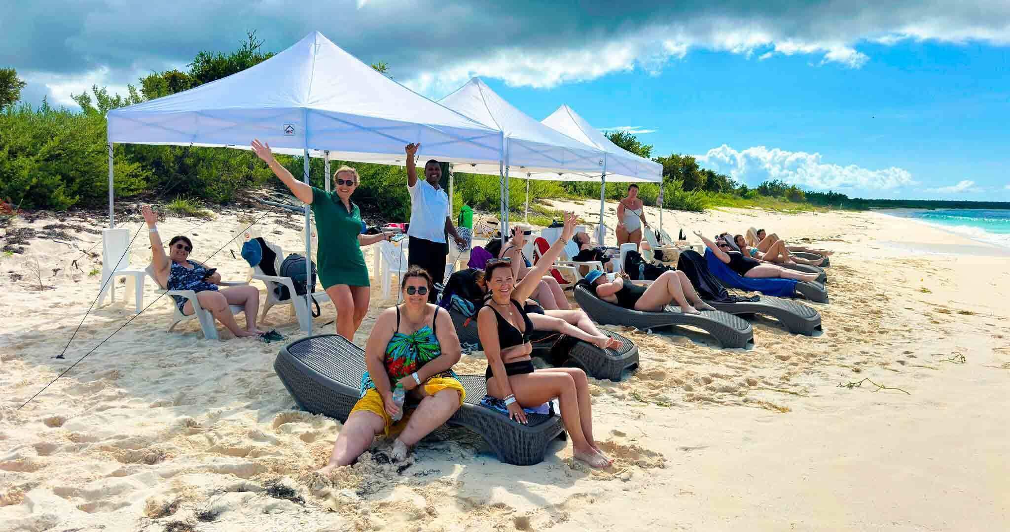 A beach with people lounging under white tents, some sitting on lounge chairs, and others on inflatable loungers.