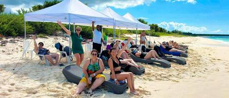 A beach with people lounging under white tents, some sitting on lounge chairs, and others on inflatable loungers.