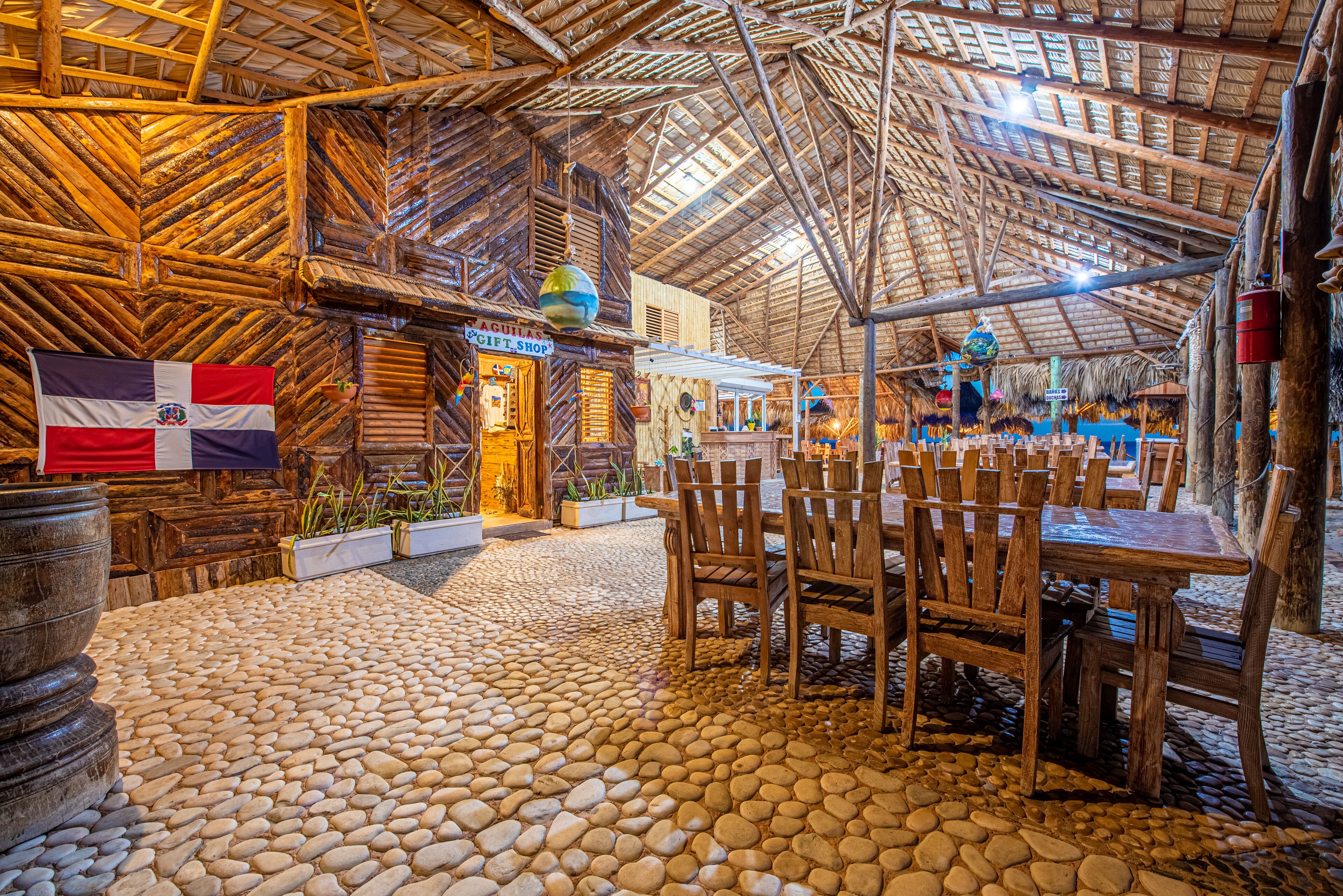 A rustic wooden structure with a thatched roof, stone flooring, and wooden furniture.