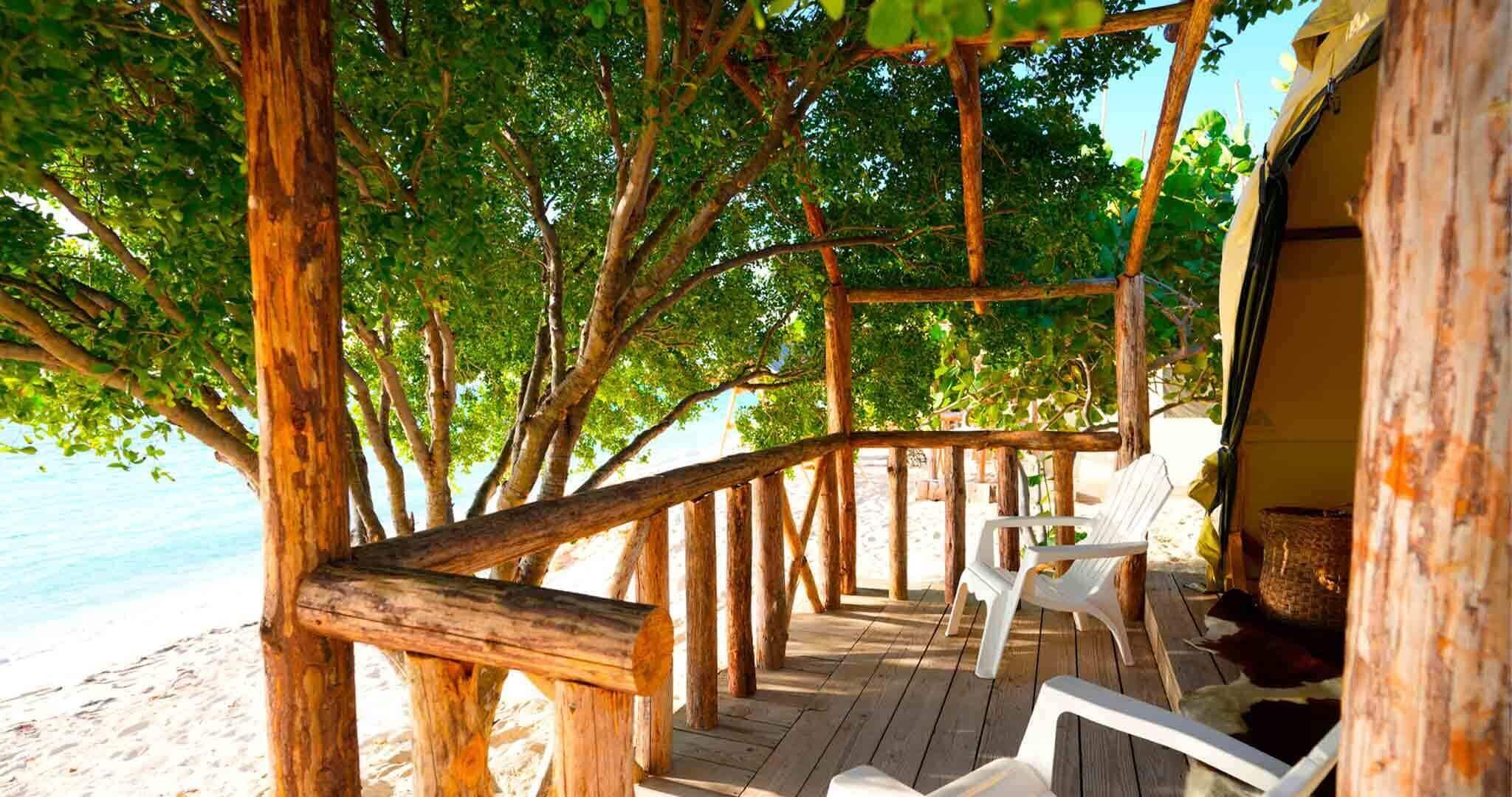 Una terraza de madera con sillas blancas, con vista a una playa y un cielo despejado.