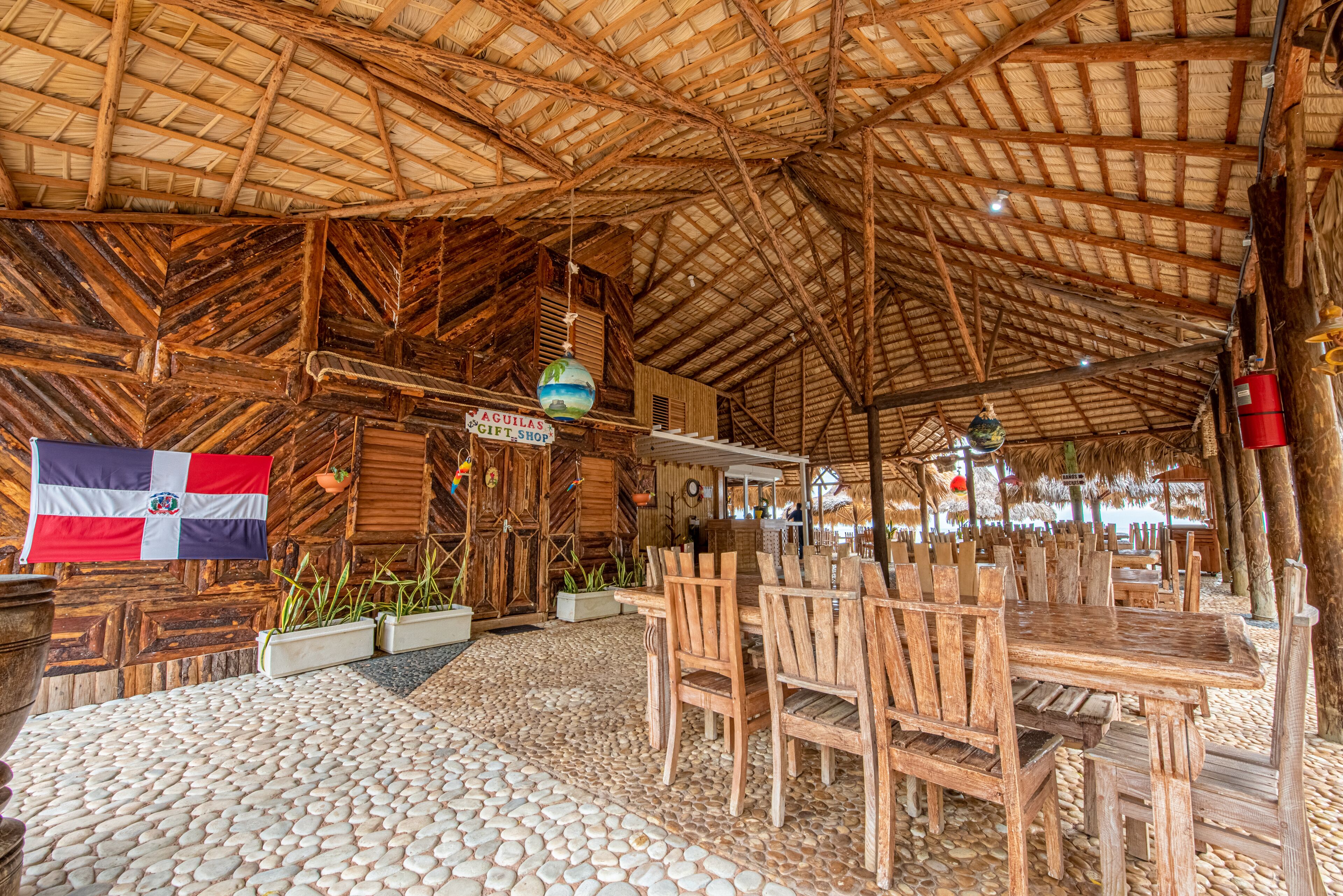 A rustic wooden structure with a thatched roof, wooden tables and chairs, and a flag.