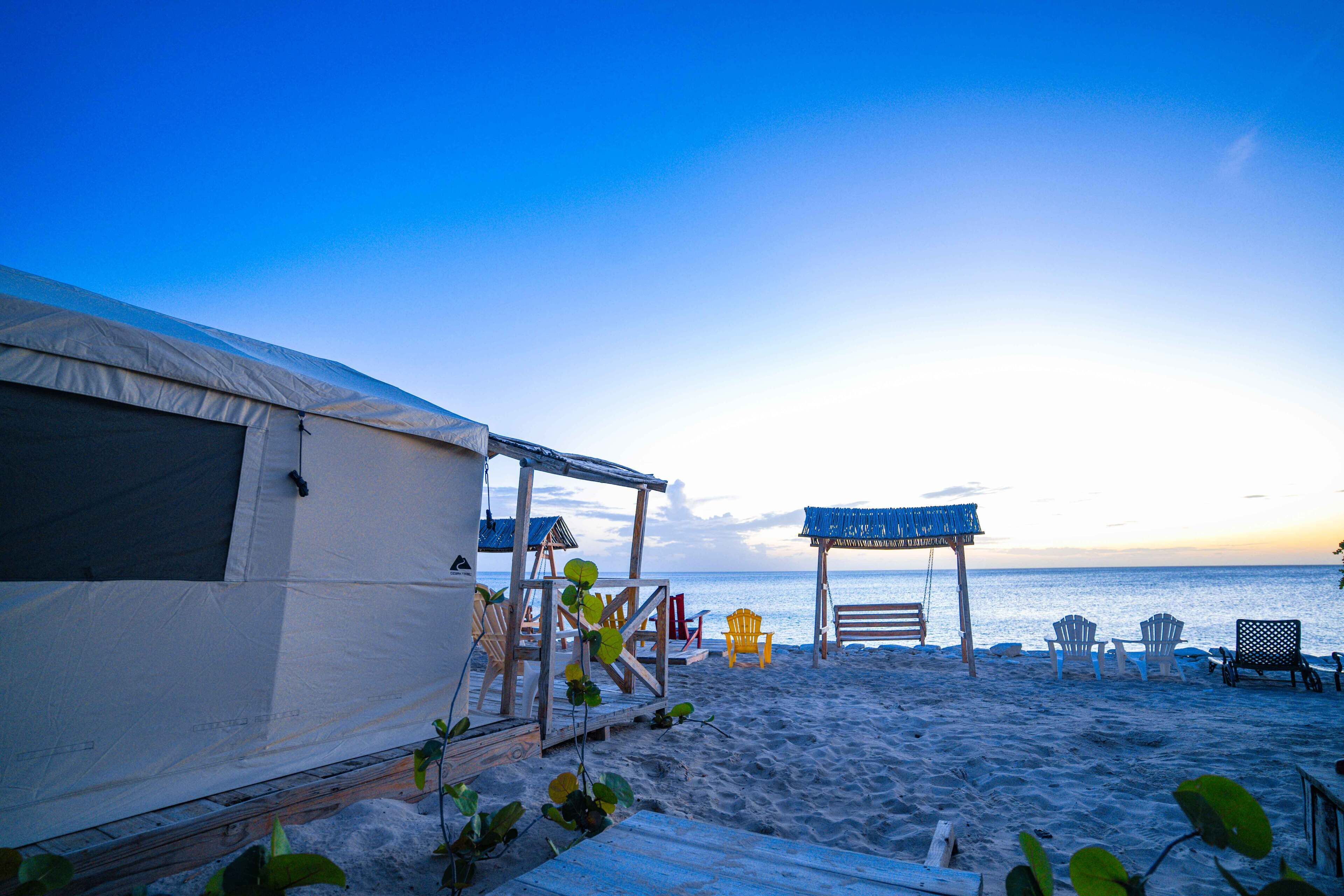 A beachside accommodation with a tent, wooden deck, and beach chairs.