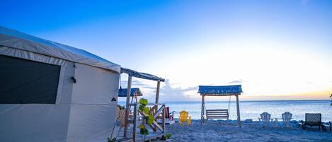 A beachside accommodation with a tent, wooden deck, and beach chairs.