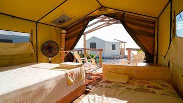 Un hébergement sous tente comprenant deux lits, un ventilateur et offrant une vue sur la plage et les bâtiments.