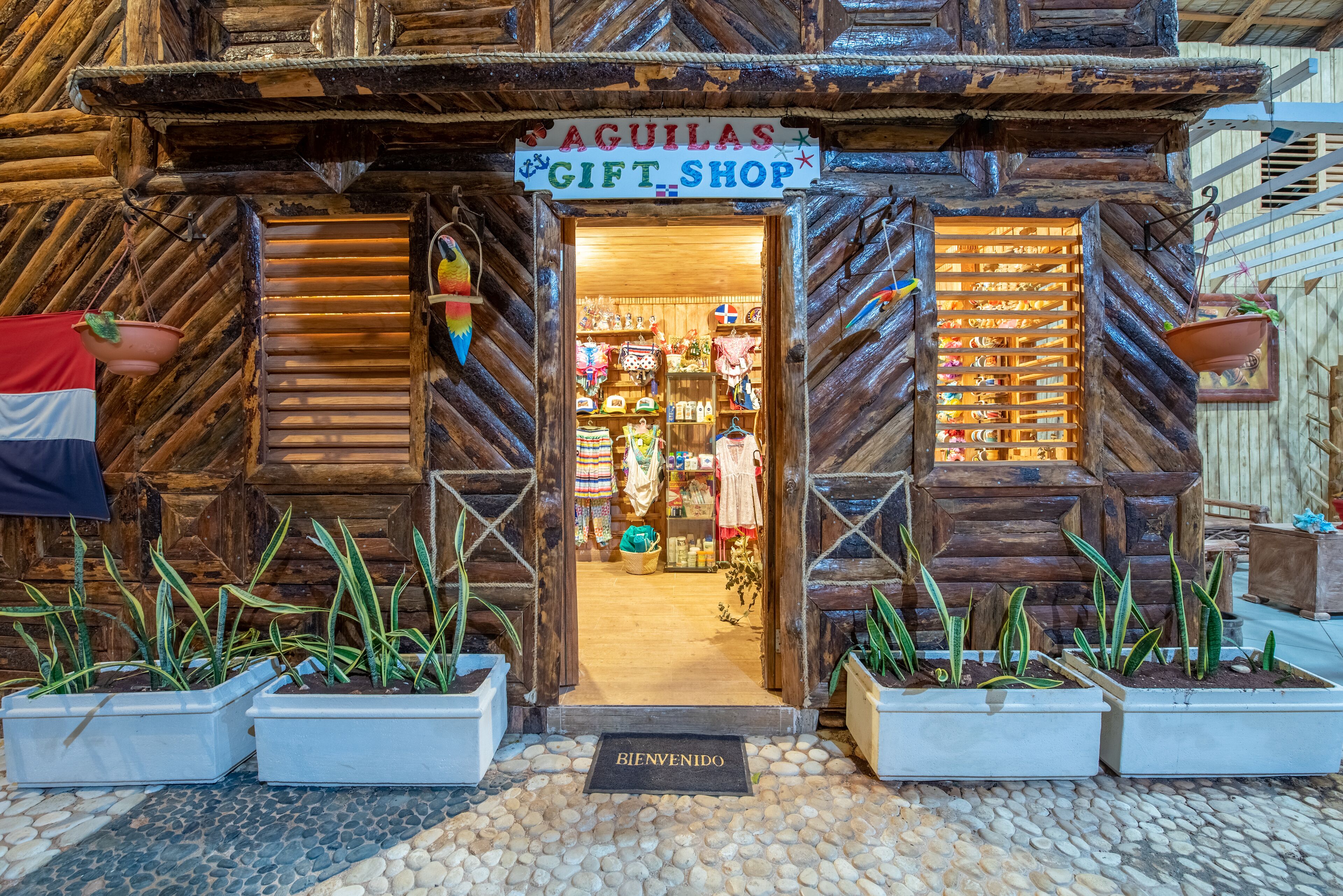 Una tienda de regalos rústica de madera llamada "AGUILAS GIFT SHOP", con fachada de madera, plantas en macetas y un felpudo.