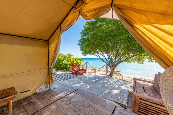 A beachside tent with a wooden deck, a red chair, and a view of the ocean. - Glamping Ecolodge Cueva de las Águilas (Pedernales)