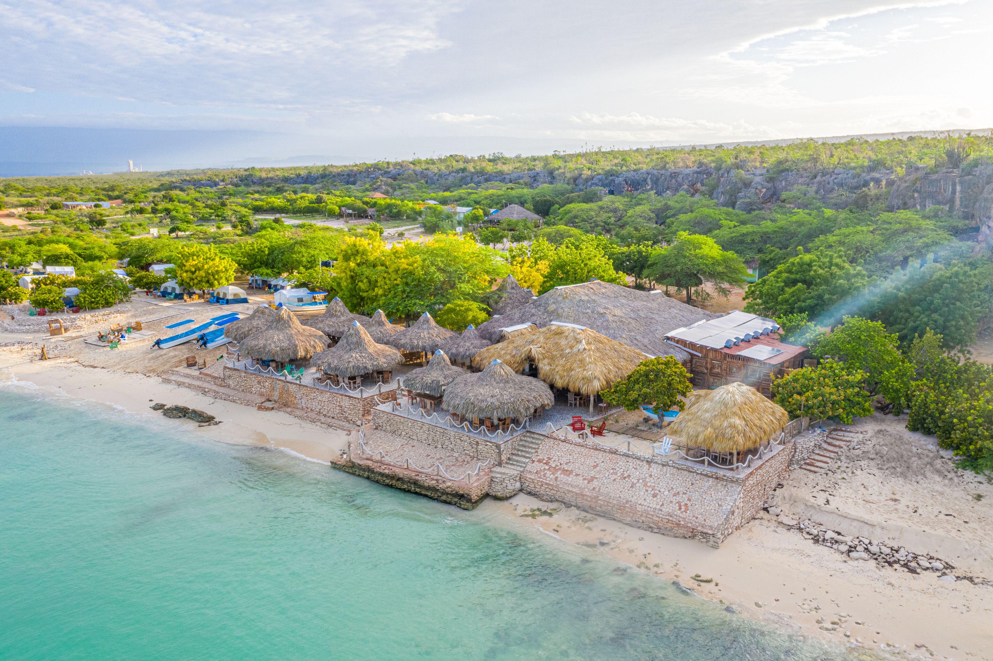 Un resort frente al mar con cabañas de techo de paja, una playa arenosa y vistas al océano.
