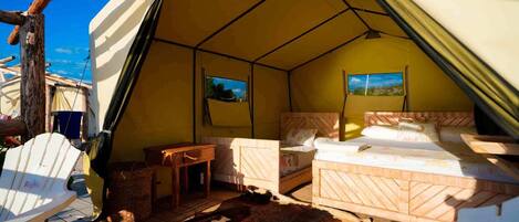 A tented accommodation with two beds, a small table, and a view of the outdoors.