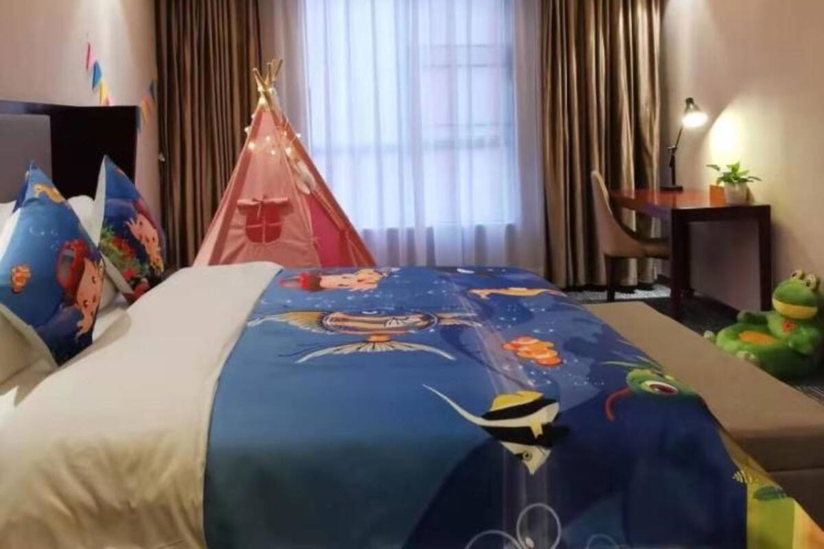 Une chambre d’hôtel avec un lit, une fenêtre avec des rideaux, une petite table avec une lampe et une tente dans un coin.