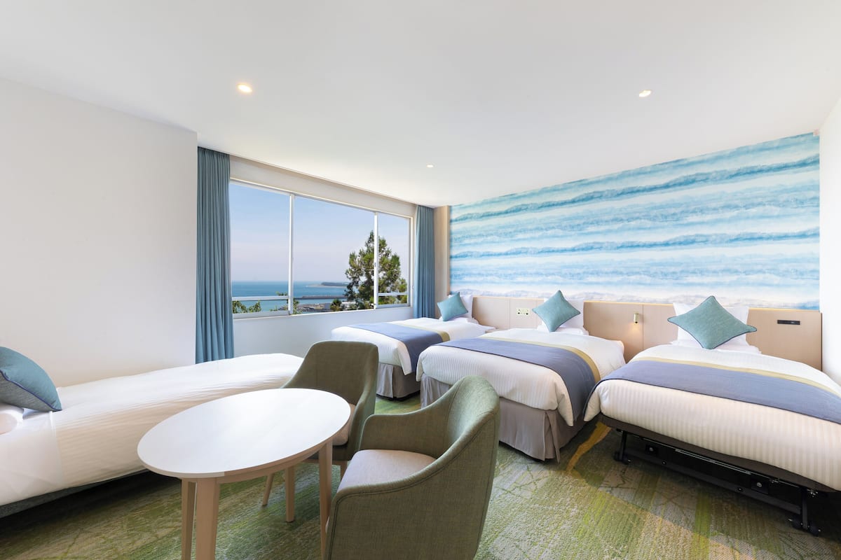 Habitación de hotel con dos camas, un sofá, una mesa y vistas al mar.