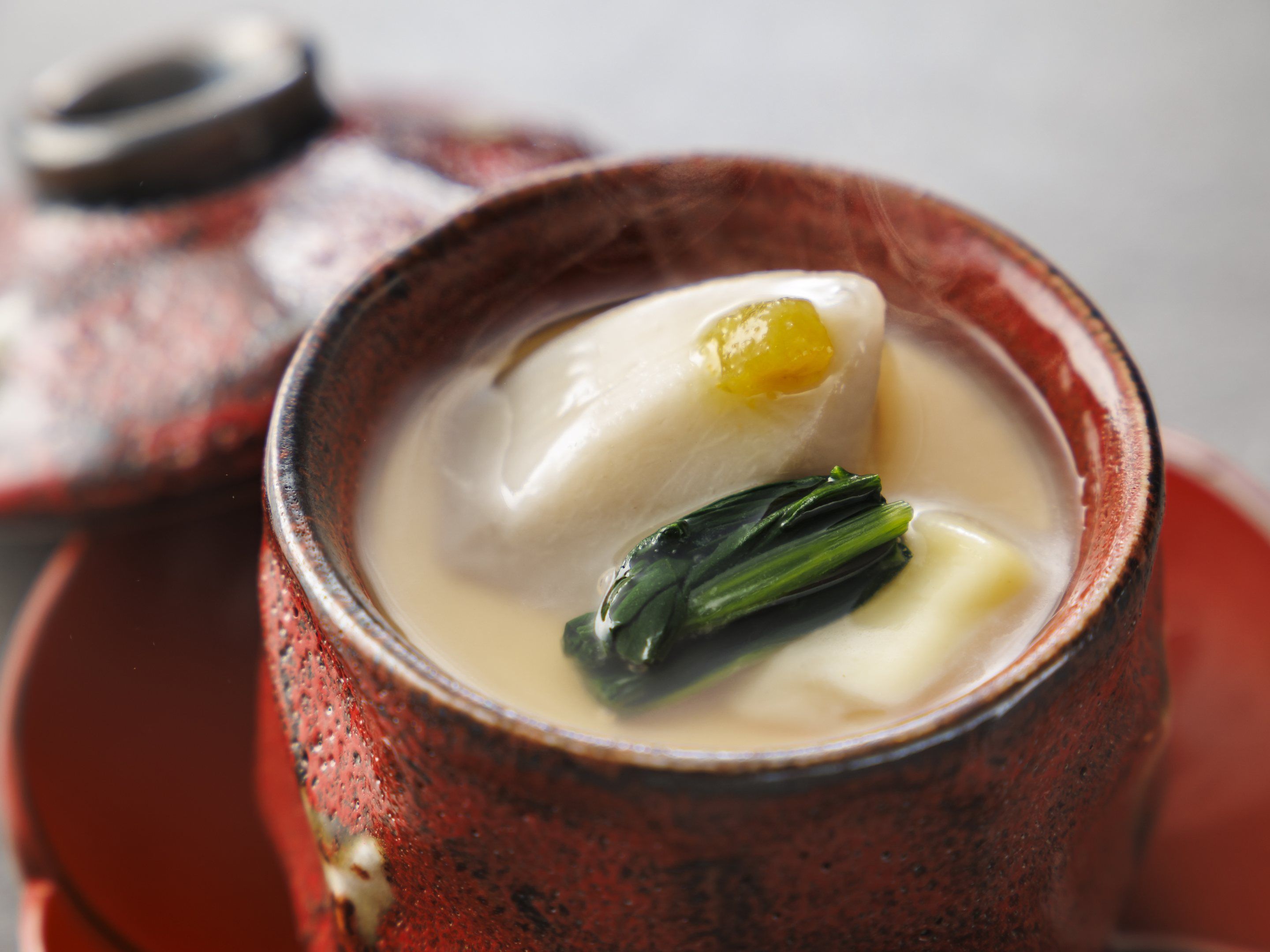 Un tazón de cerámica con una sopa cremosa que contiene un buñuelo y verduras de hoja verde.