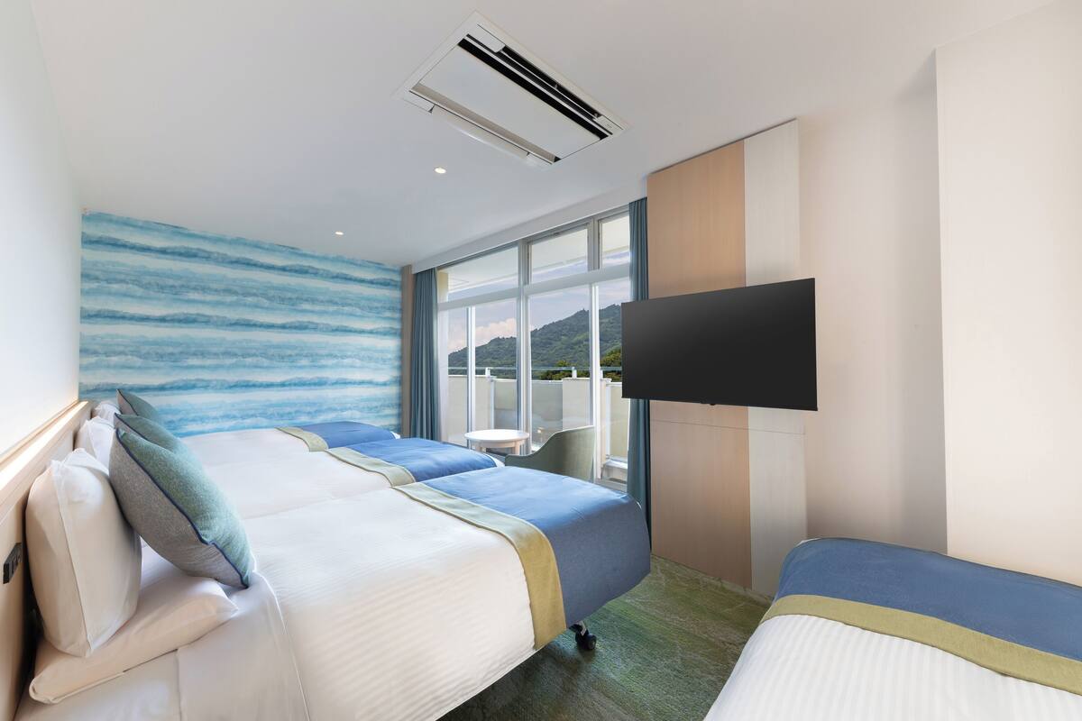 Habitación de hotel con dos camas, un ventanal con vistas, un televisor de pantalla plana y un equipo de aire acondicionado.