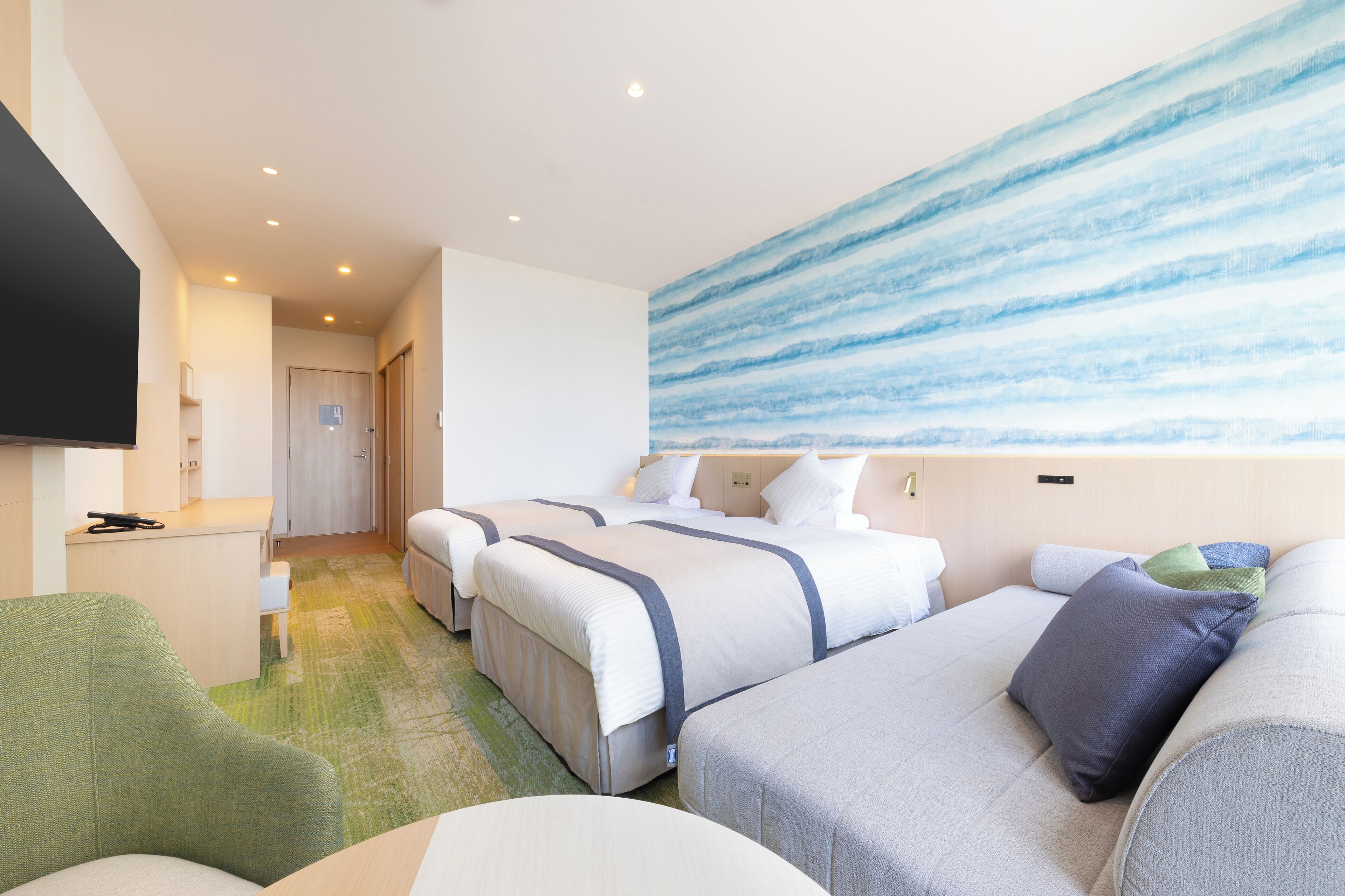 A hotel room with two beds, a green armchair, a flat-screen TV, and a large abstract painting on the wall.
