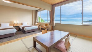 Habitación de hotel con dos camas, una mesa de comedor y vista al océano.