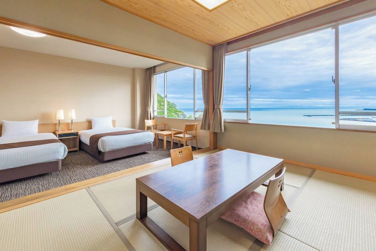 Habitación de hotel con dos camas, una mesa de comedor y vista al océano.