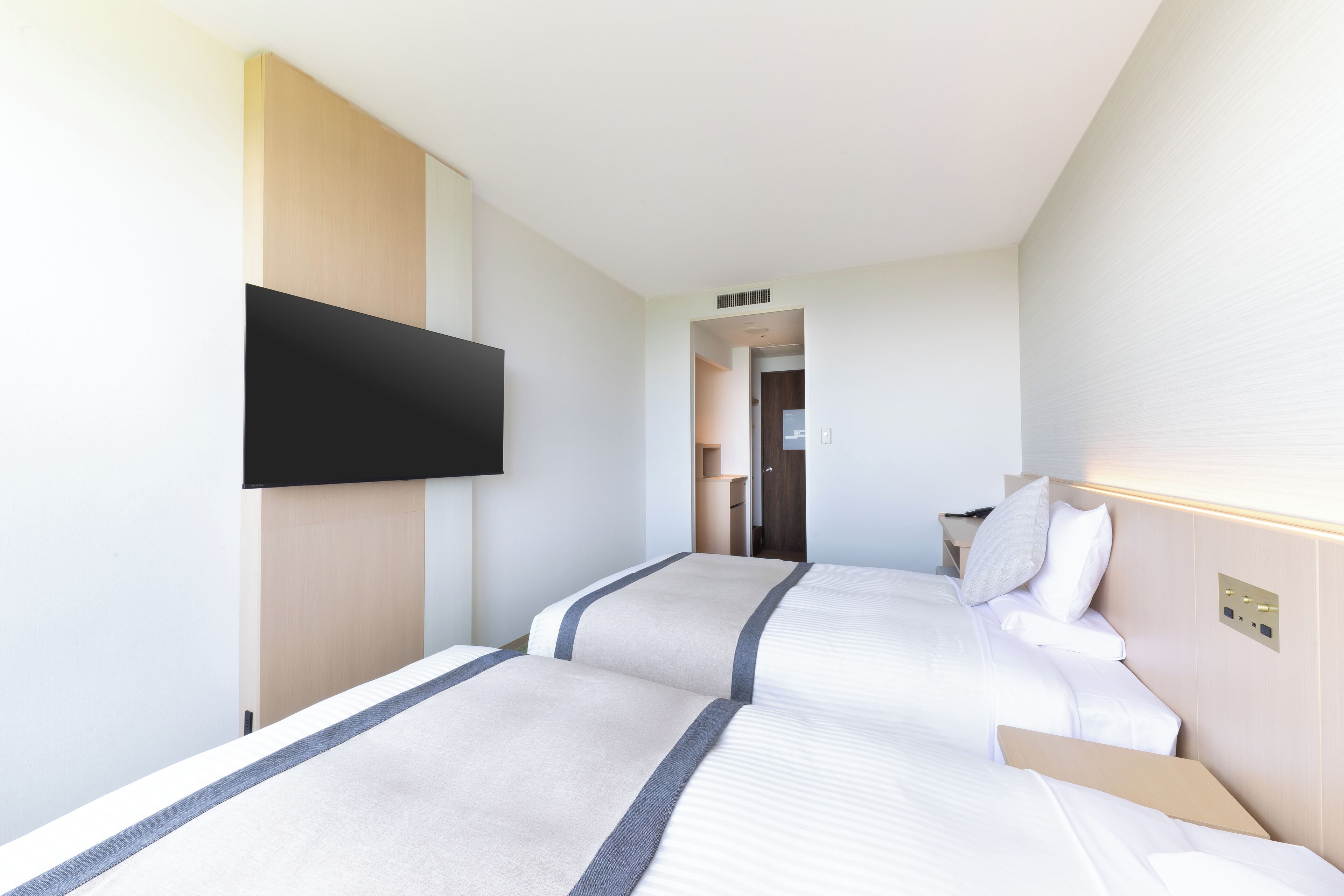 Habitación de hotel con dos camas, un televisor de pantalla plana montado en la pared y una puerta que da a un baño.