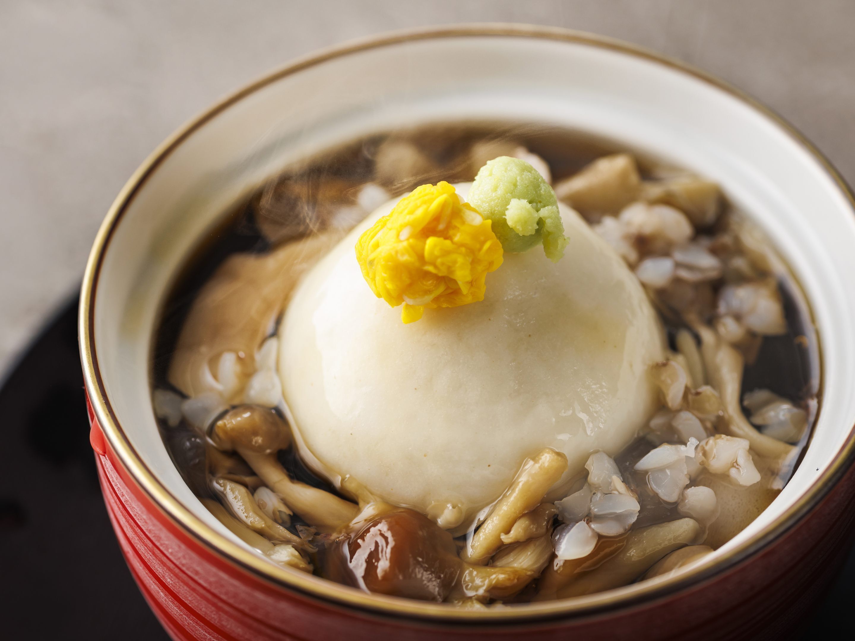 A bowl of soup with a dumpling and a flower garnish.