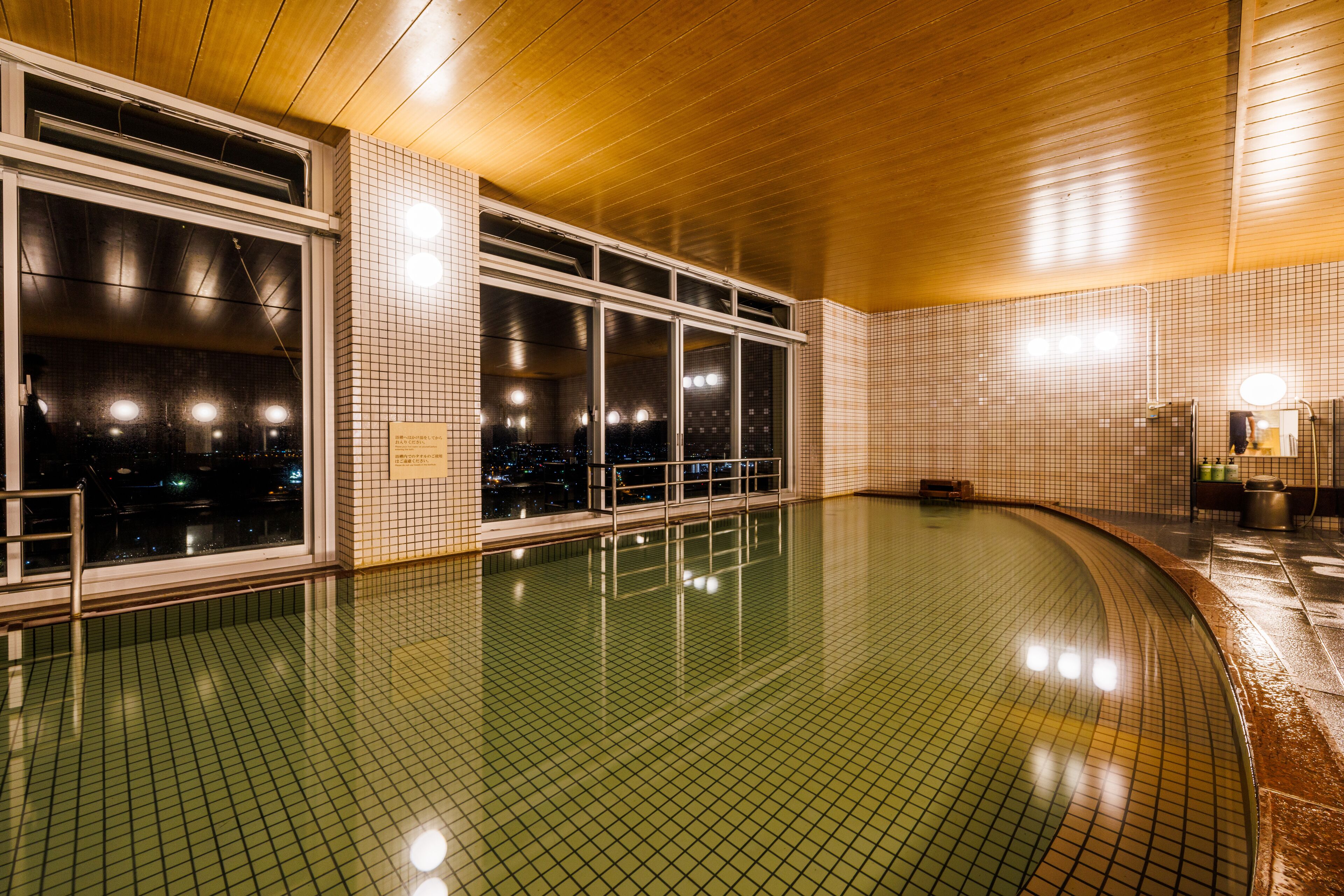 Una piscina con paredes de azulejos y techo de madera, ventanas amplias y un banco.