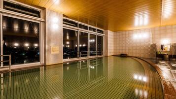 Una piscina con paredes de azulejos y techo de madera, ventanas amplias y un banco.