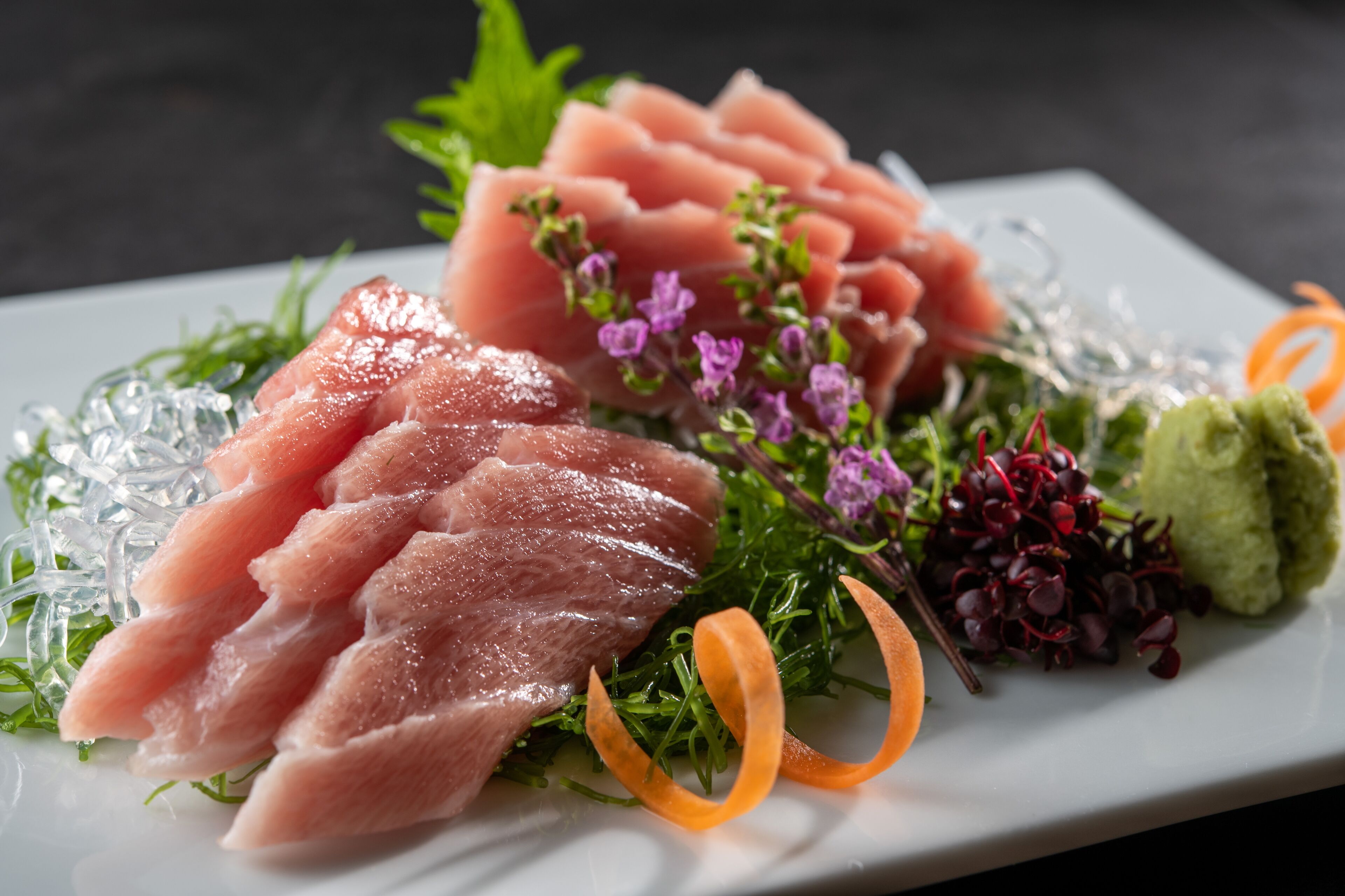 Une assiette de poisson tranché, garnie de verdure et de fleurs.
