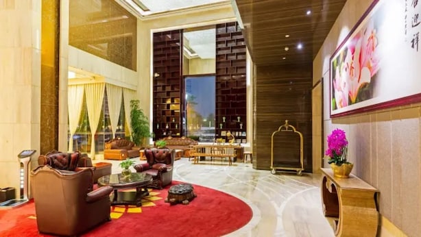 A spacious lobby with a red carpet, leather sofas, a coffee table, and a bookshelf.