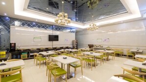 A spacious dining area with multiple tables and chairs, a flat-screen TV mounted on the wall, and a ceiling with a geometric pattern.
