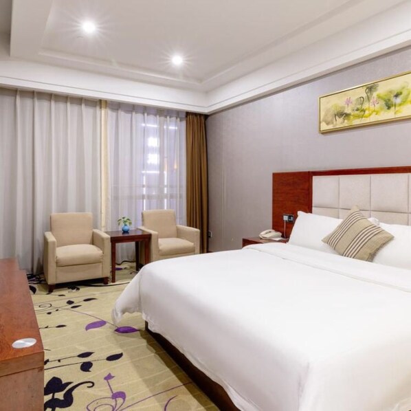 A hotel room with a large bed, two armchairs, a small table, and a painting on the wall. - Vyluk J Hotel Lucky City Lecong Foshan (Foshan)