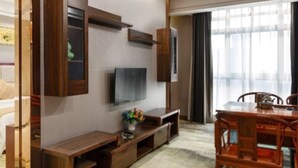 A modern living room with a flat-screen TV mounted on the wall, wooden furniture, and a large window providing natural light.