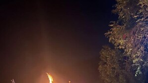 Un grupo de personas sentadas en bancos de madera alrededor de una fogata por la noche.
