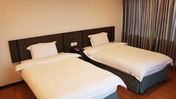 Quarto de hotel com duas camas de solteiro, cabeceira de madeira, cortina e piso de madeira.