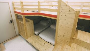 Habitación con literas de madera, un colchoneta roja en la parte superior y una puerta a la izquierda.