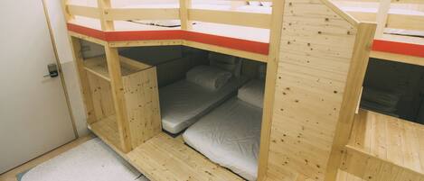 A bunk bed room with a wooden frame, a red mat at the top, and a door on the left.