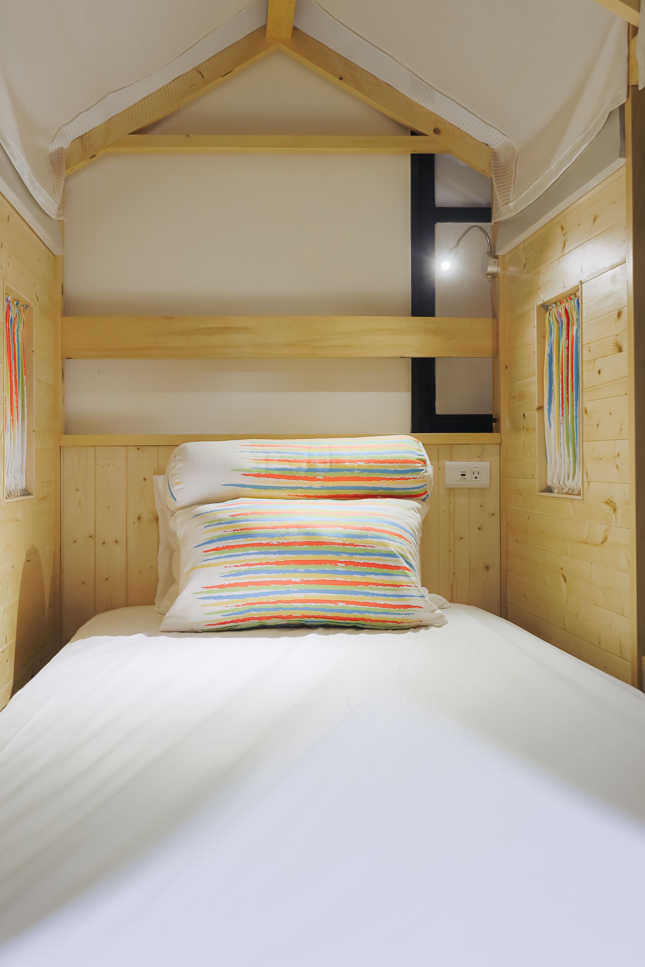 A wooden cabin room with a bunk bed, a small window, and a wall-mounted light fixture.