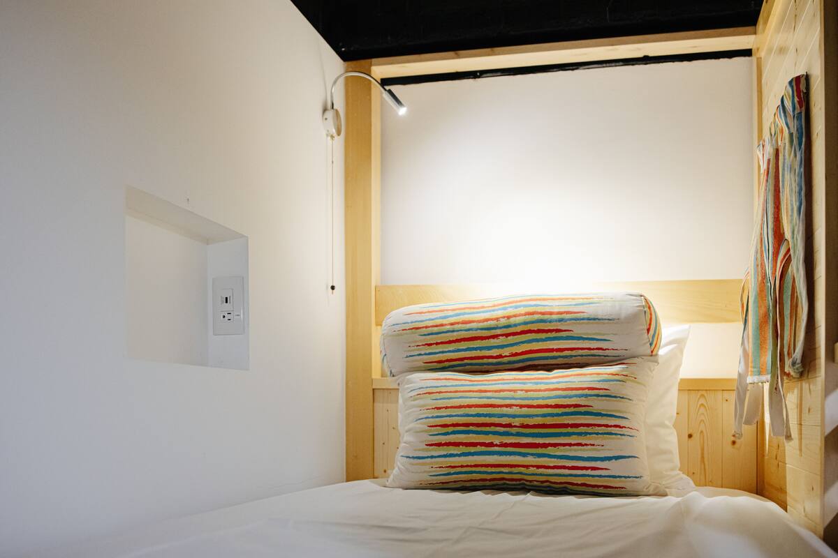 Ein Einzelbett mit Holz-Kopfteil, einer Wandsteckdose und einer Pendelleuchte.