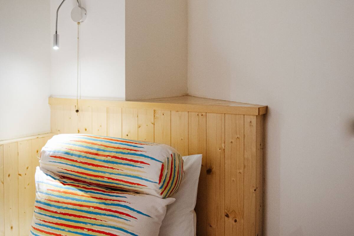 Ein Bett mit Holz-Kopfteil, einer weißen Wand und einer einzelnen Nachttischlampe.