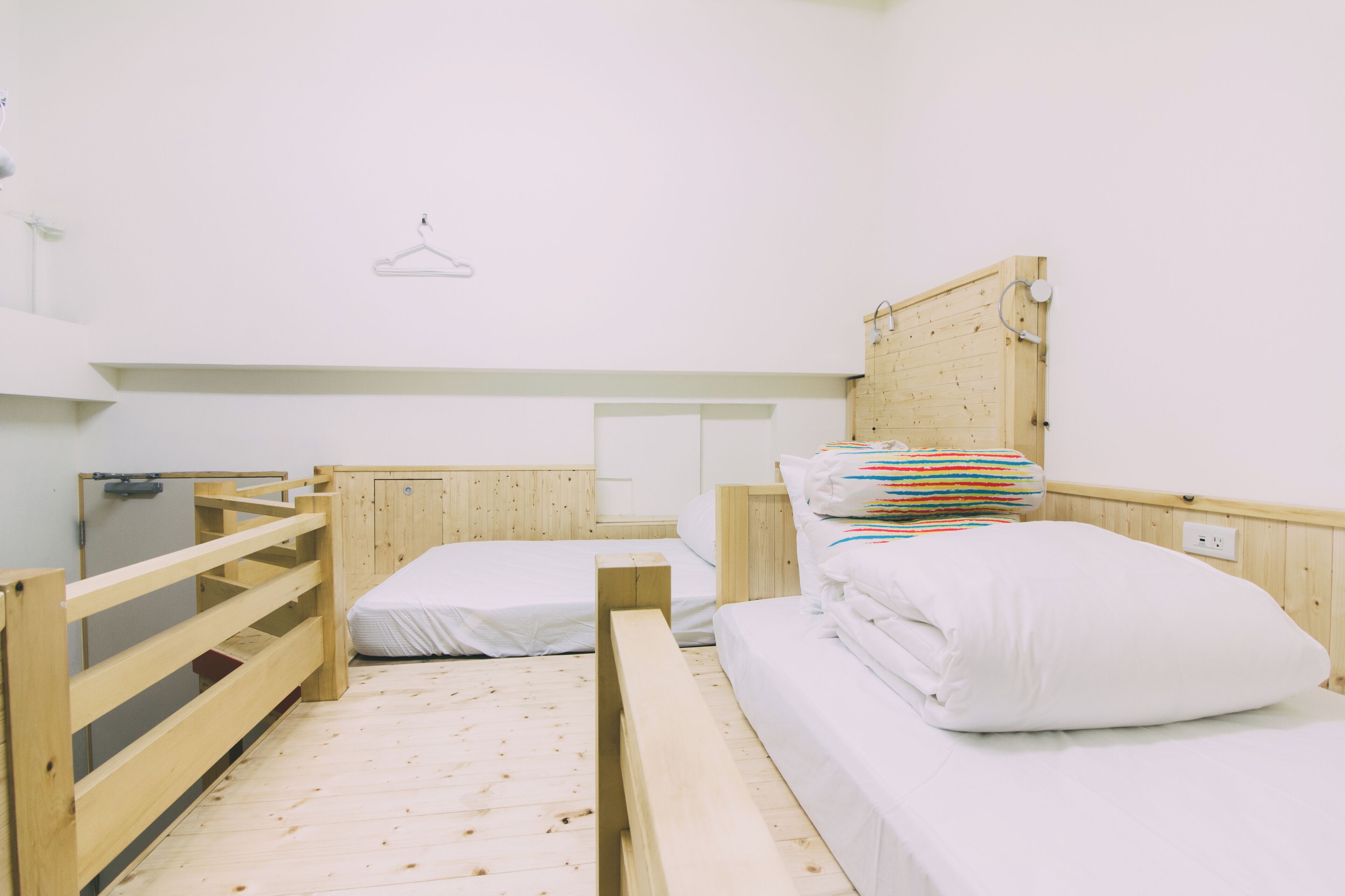 Una camera del dormitorio con letti a castello, pavimento in legno e una parete bianca spoglia con un appendiabiti.