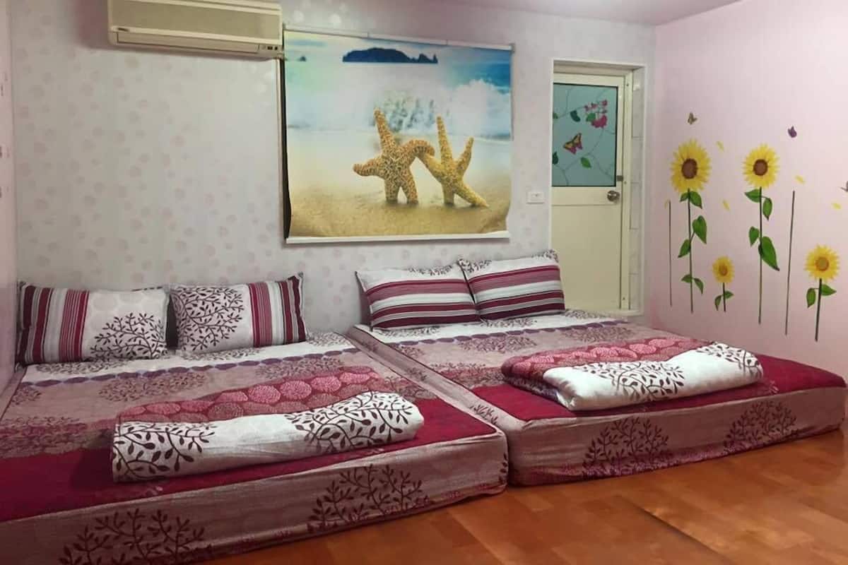 A bedroom with two beds, patterned bedding, a wall-mounted air conditioner, a painting of giraffes, and a door with a floral decal.