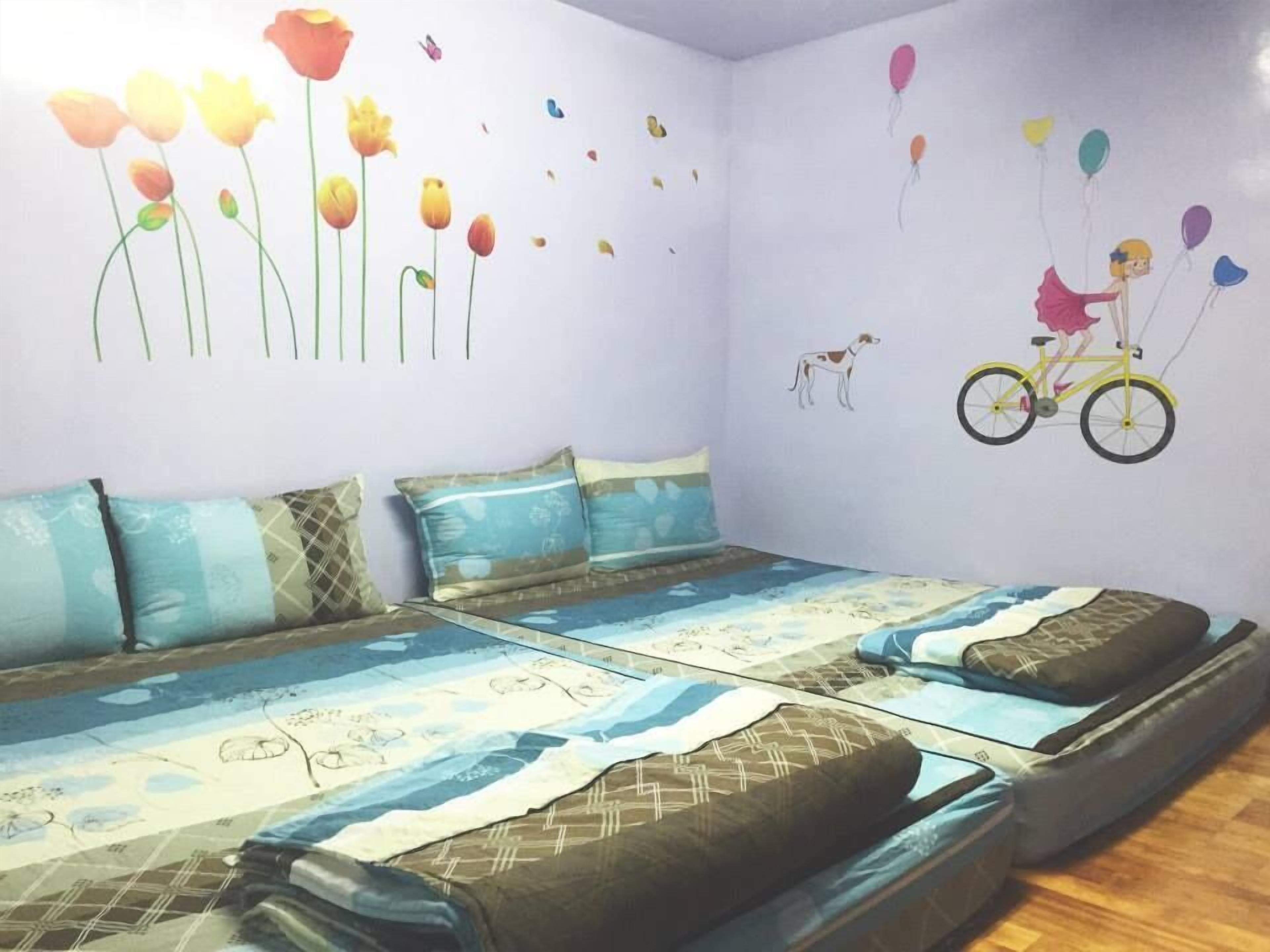 A room with two beds, patterned bedding, and wall decorations including flowers and a bicycle.