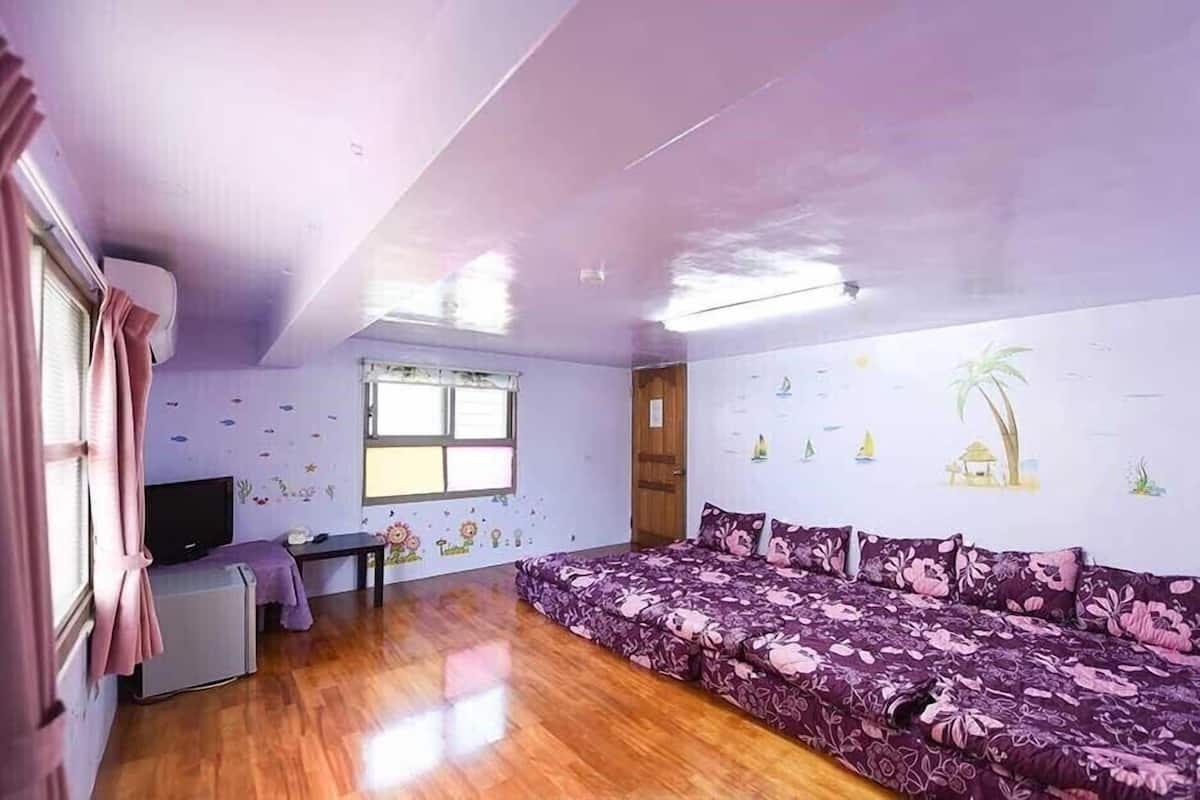 A room with a wooden floor, a sofa, a TV, and a window with curtains.