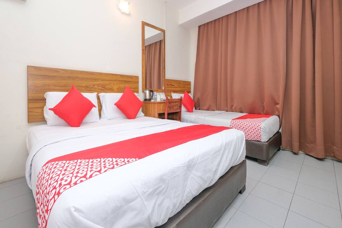 Ein Hotelzimmer mit zwei Betten, einem Holzkopfende, einem Nachttisch, einem Spiegel und braunen Vorhängen.