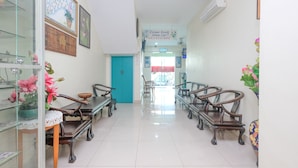 A hallway with a blue door, wooden chairs, a table with a lace tablecloth, and a glass display case with flowers. - OYO 89877 Sun Triang Hotel (Teriang)