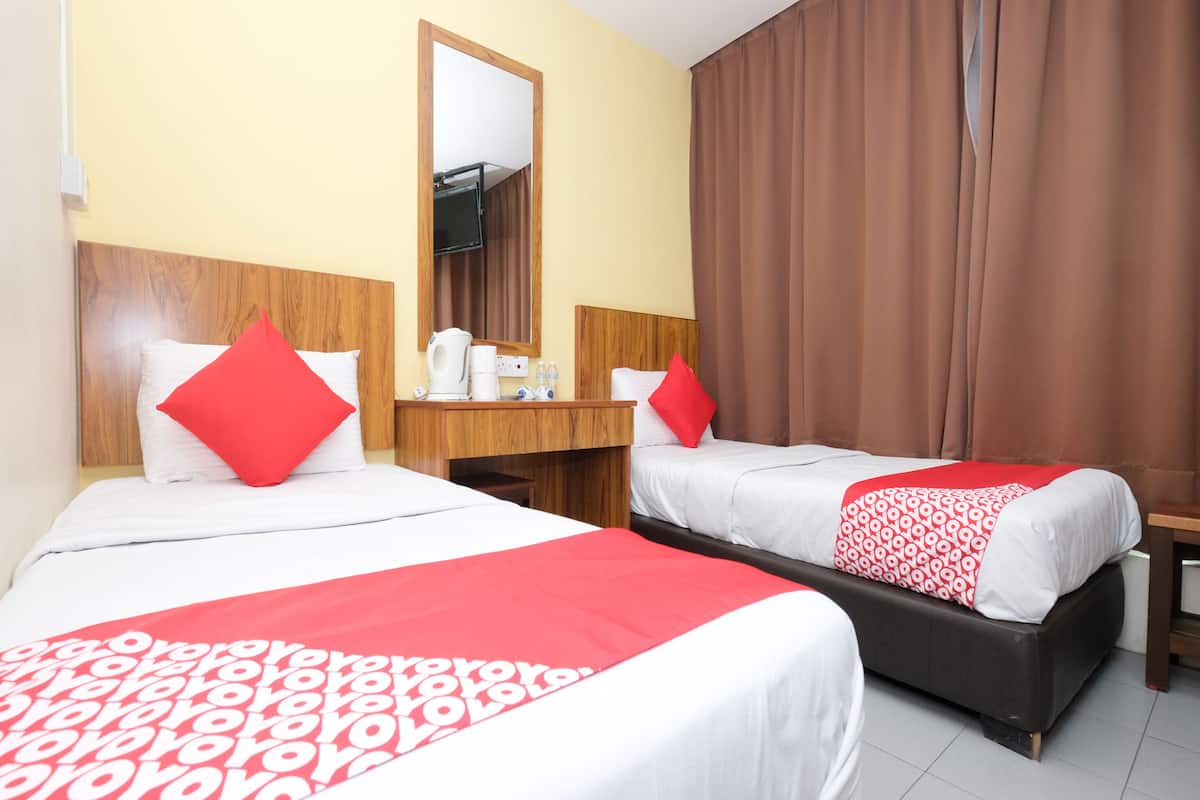 Ein Hotelzimmer mit zwei Betten, jeweils mit roter und weißer Bettwäsche, einem hölzernen Kopfteil, einem Nachttisch mit Wasserkocher und einem Spiegel.