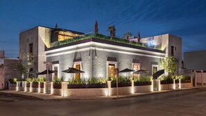 A modern building with a flat roof, outdoor seating area with umbrellas, and a well-lit entrance. - Diez Diez Collection (Mérida)