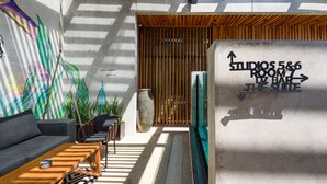 A modern interior with a sofa, chairs, a table, and a wall with directional signage for 'STUDIOS 5&6 ROOM 7' and 'THE SOLE BAR'. - Diez Diez Collection (Mérida)