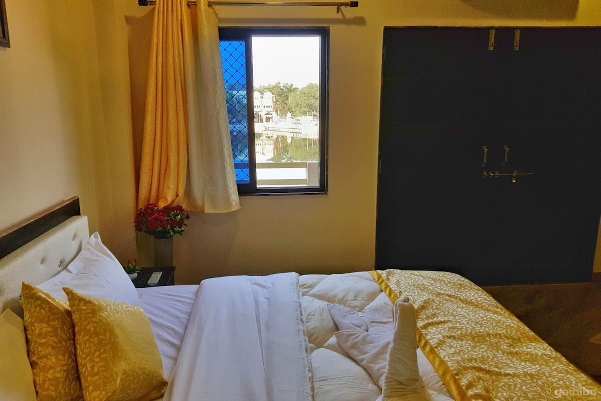 A hotel room with a bed, a window with a view of buildings, a door, and a curtain.