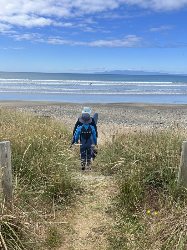 Un sentier qui mène à une plage, où l  ’on voit une personne en combinaison de plongée se dirigeant vers l’eau.