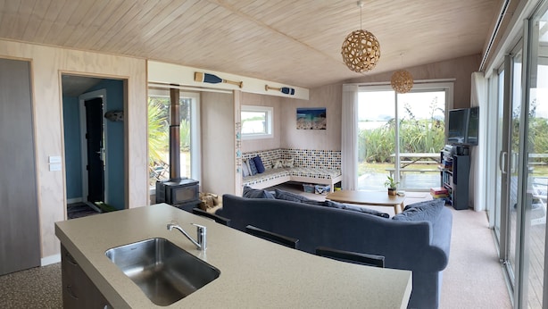 A modern kitchen with a large island, a built-in seating area with a blue sofa, and a dining table. - Surfs up beach Bach  (Colac Bay)